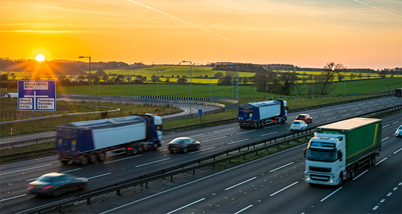 sunset over highway with trucks and cars driving through lush green landscape showcasing evening commute and transportation options on route to 10 destinations