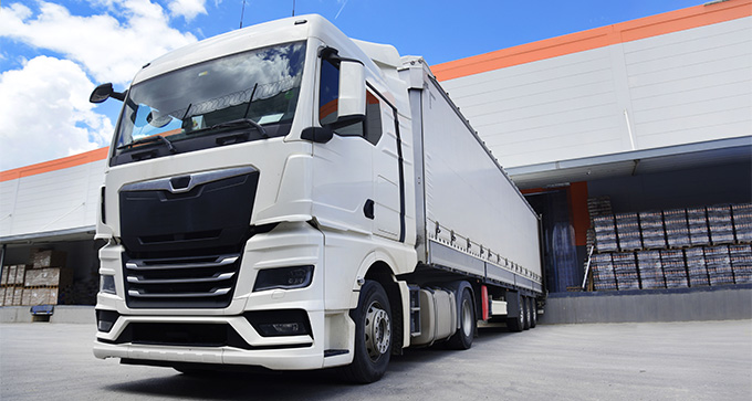 white truck parked near warehouse loading dock with clear blue sky and nine pallets of goods in the background