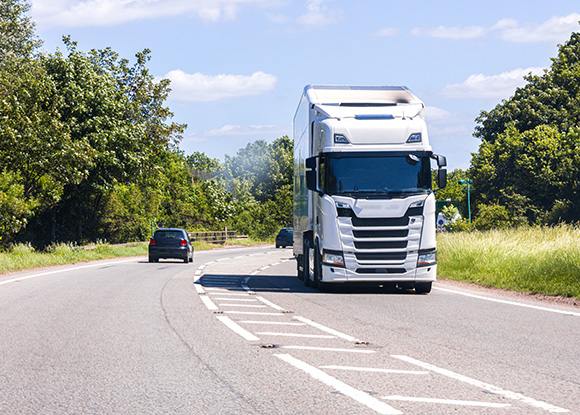 large white truck driving on a rural road with green trees visible in the background delivering goods multiple lanes and a clear blue sky